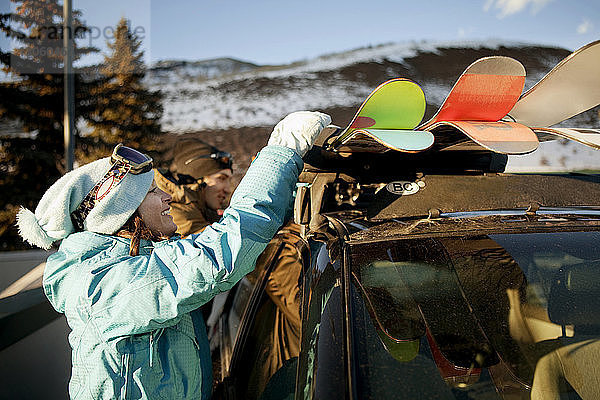 Seitenansicht einer Frau  die Skier aus dem Auto nimmt  während sie bei einem Freund im Skigebiet steht