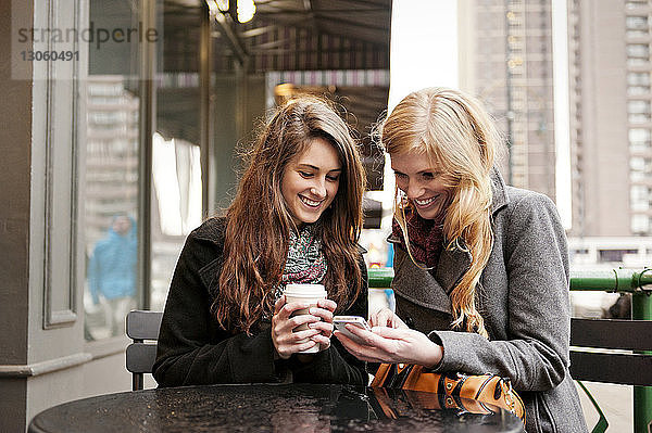 Glückliche Freunde telefonieren  während sie im Straßencafé sitzen