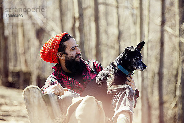 Nachdenklicher Mann sitzt mit Hund auf Bank im Wald während des Urlaubs