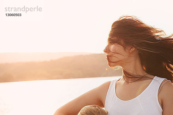 Frau mit zerzaustem Haar bei Sonnenuntergang gegen See