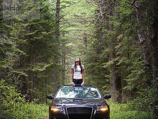Frau steht im Auto inmitten von Bäumen am Wald