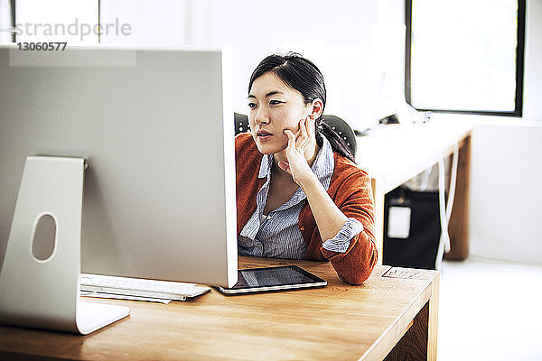 Geschäftsfrau  die am Computer arbeitet  während sie im Büro am Tisch sitzt