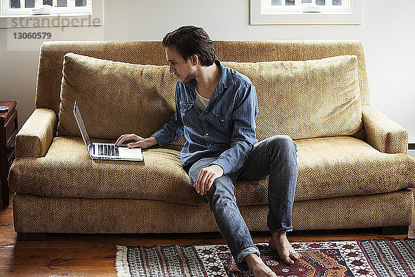 Mann benutzt Laptop-Computer  während er zu Hause auf dem Sofa sitzt