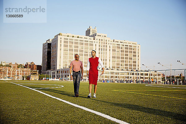 Mann und Vater gehen bei Sonnenschein auf dem Fussballfeld