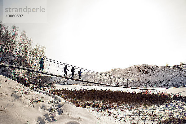 Freunde gehen im Winter bei klarem Himmel auf einer Fußgängerbrücke