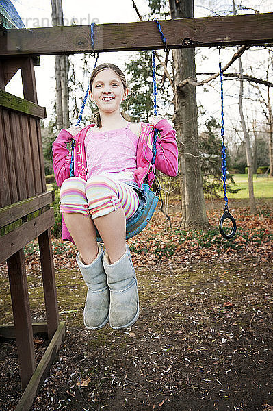 Porträt eines lächelnden Mädchens  das sich auf dem Spielplatz über das Feld schwingt