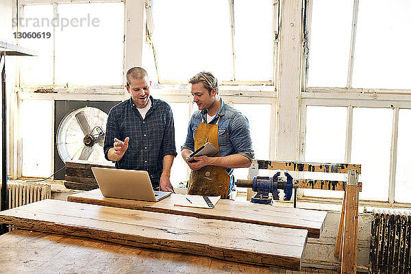 Männliche Schreiner schauen auf den Laptop und diskutieren in der Werkstatt