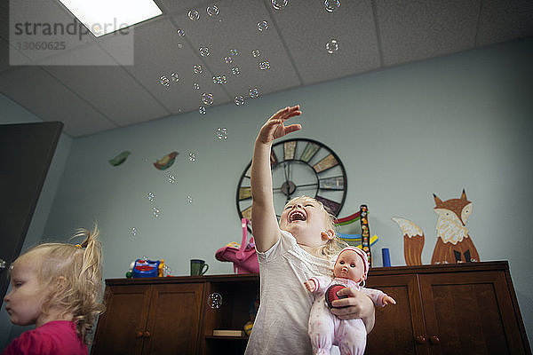Niedrigwinkelansicht eines fröhlichen Mädchens  das in der Vorschule mit Blasen spielt