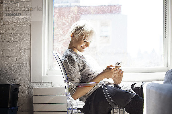 Seitenansicht einer glücklichen Frau  die zu Hause ein Smartphone benutzt