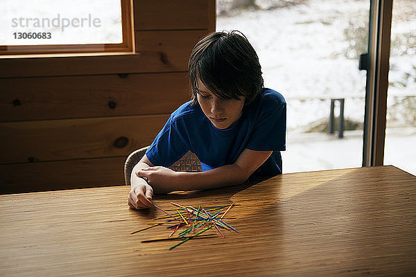 Junge spielt zu Hause am Tisch mit Stöcken