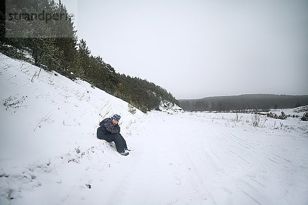 Teenager sitzt auf schneebedecktem Feld gegen den Himmel