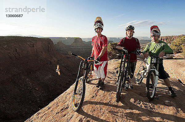 Porträt von Mountainbikern mit Fahrrädern  die auf einer Klippe stehen