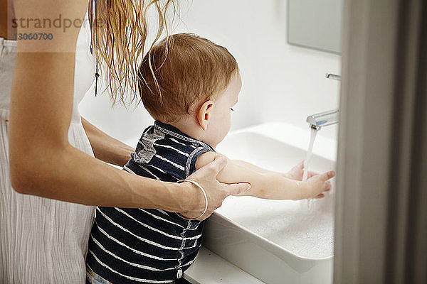 Ausgeschnittenes Bild einer Mutter  die dem Baby beim Händewaschen hilft