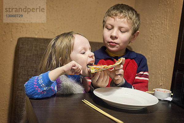 Bruder gibt Schwester am Tisch Pizza zu essen