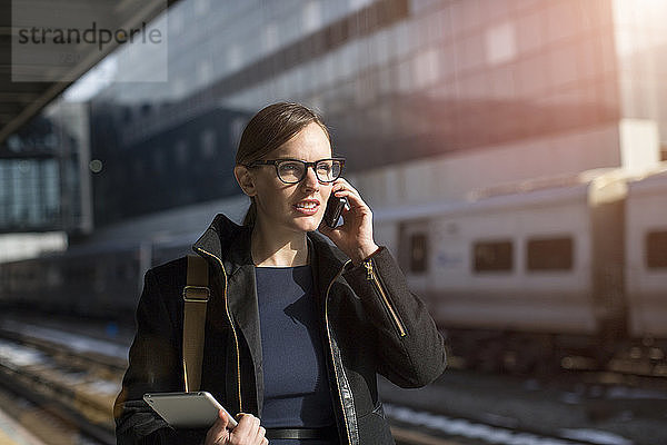 Geschäftsfrau telefoniert  während sie am Bahnsteig des Bahnhofs steht