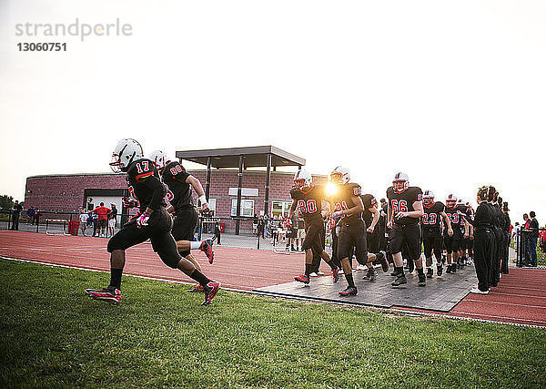 Männliche American-Football-Spieler rennen auf dem Spielfeld gegen den klaren Himmel