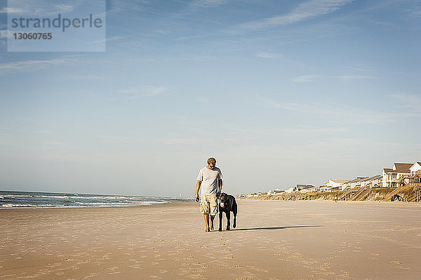 Mann geht mit Hund am Ufer gegen den Himmel