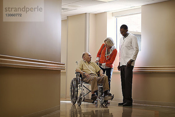 Frau mit Arzt steht Mann auf Rollstuhl im Krankenhaus zur Seite