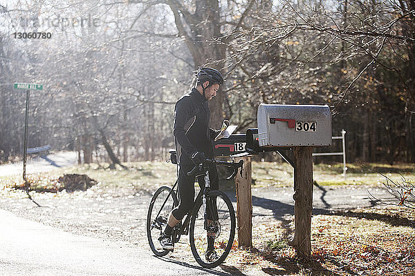 Radfahrer mit Fahrrad  der an sonnigen Tagen Briefe aus dem Briefkasten nimmt