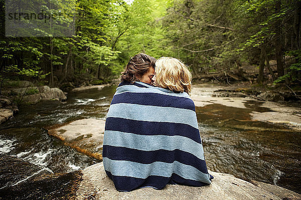 In ein Handtuch gewickeltes Paar sitzt auf Felsen im Fluss