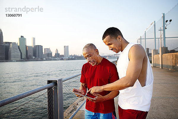 Mann und Vater benutzen Tablet-Computer  während sie auf der Promenade am East River in der Stadt stehen