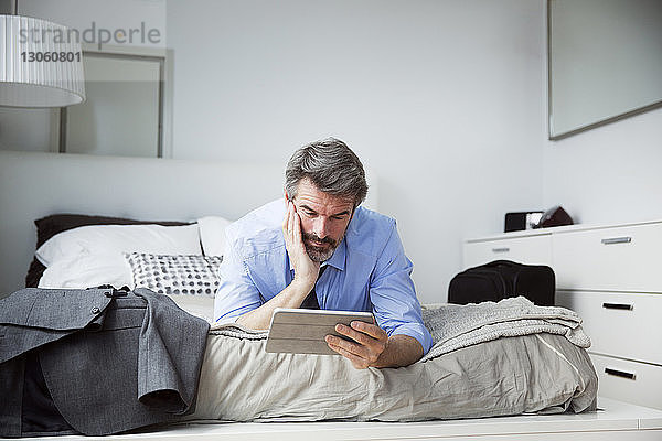Geschäftsmann schaut auf Tablet-Computer  während er im Hotelzimmer auf dem Bett liegt