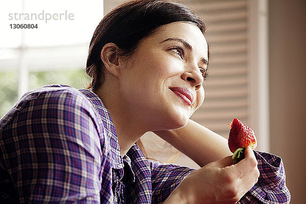 Glückliche Frau schaut weg  während sie eine Erdbeere hält