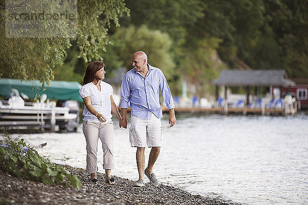 Glückliches Paar hält sich beim Spaziergang am Seeufer an den Händen
