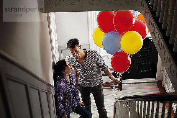 Hochwinkelaufnahme eines Mannes  der Heliumballons hält  während er bei einer Frau zu Hause steht