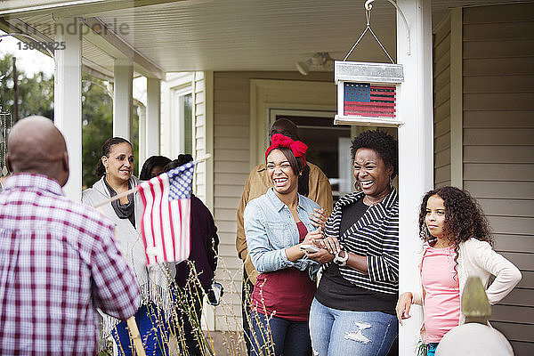 Glückliche Frauen schauen einen Mann mit amerikanischer Flagge vor dem Haus an