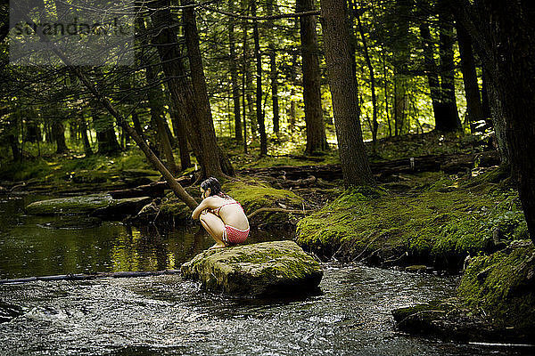 Rückansicht eines Mädchens  das auf einem Felsen im Fluss sitzt