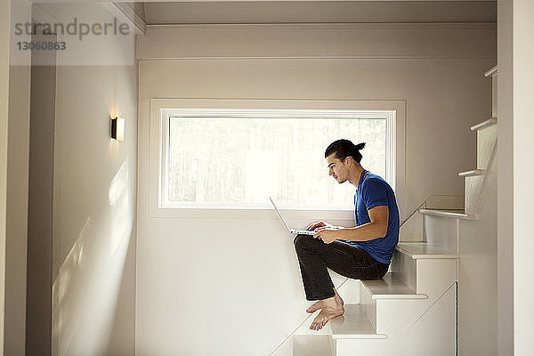 Mann benutzt Laptop-Computer  während er zu Hause auf Stufen sitzt