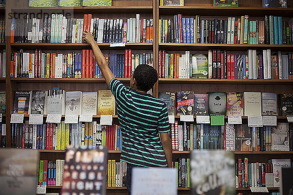 Rückansicht eines Mannes  der ein Buch aus dem Regal nimmt  während er im Laden steht