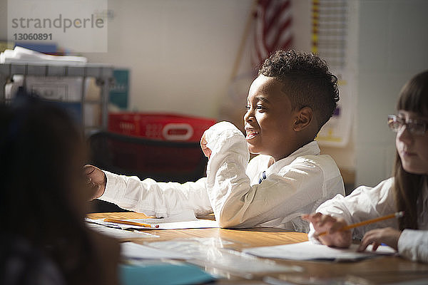 Fröhlicher Schuljunge sitzt mit Mädchen am Schreibtisch im Klassenzimmer