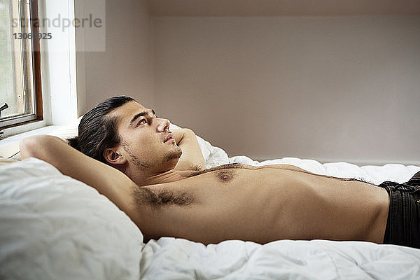 Mann ohne Hemd schaut weg  während er zu Hause auf dem Bett liegt
