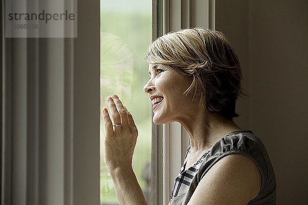 Fröhliche Frau schaut zu Hause durchs Fenster