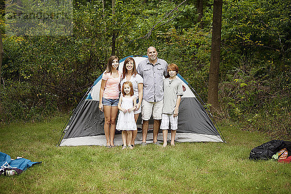Porträt einer glücklichen Familie  die im Wald vor einem Zelt steht