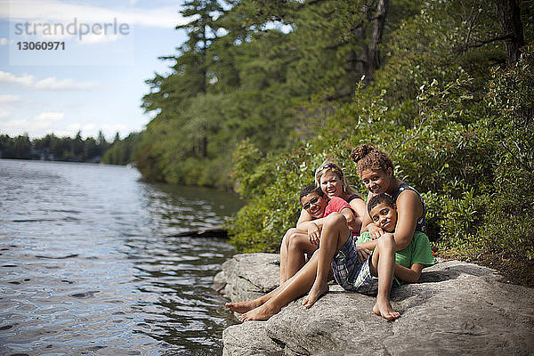 Porträt einer auf einem Felsen am See sitzenden Familie