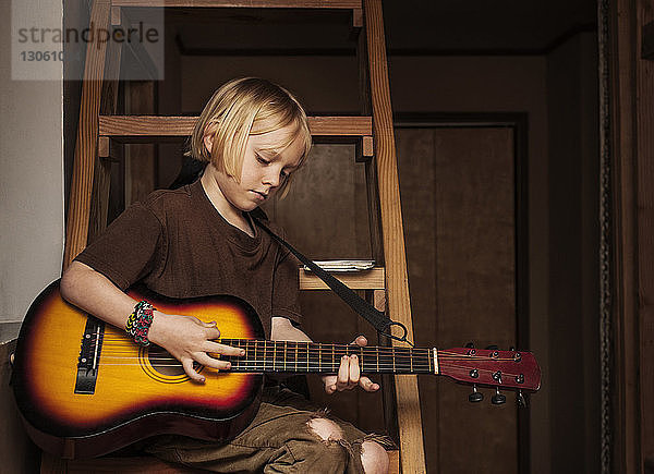 Junge übt Gitarre  während er zu Hause auf der Leiter sitzt