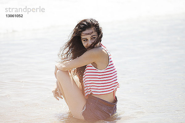 Seitenansicht einer nachdenklichen Frau  die am Strand am Ufer sitzt