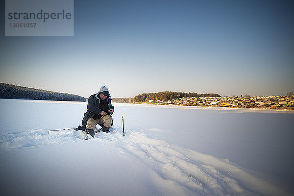 Mann Eisfischen auf gefrorenem See bei klarem Himmel