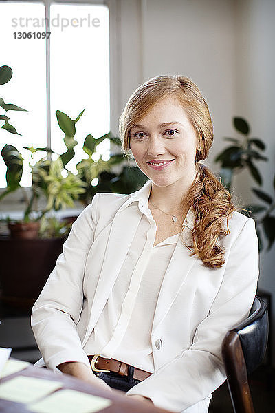 Porträt einer selbstbewusst lächelnden Geschäftsfrau  die im Büro sitzt