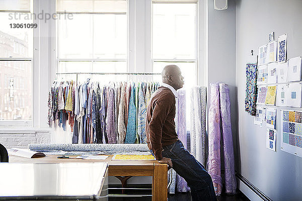 Seitenansicht eines männlichen Modedesigners  der in einem Workshop Entwürfe an der Wand betrachtet