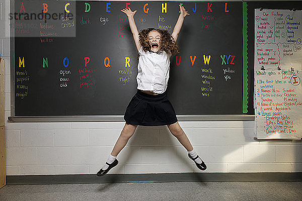 Aufgeregtes Schulmädchen springt im Klassenzimmer gegen die Tafel