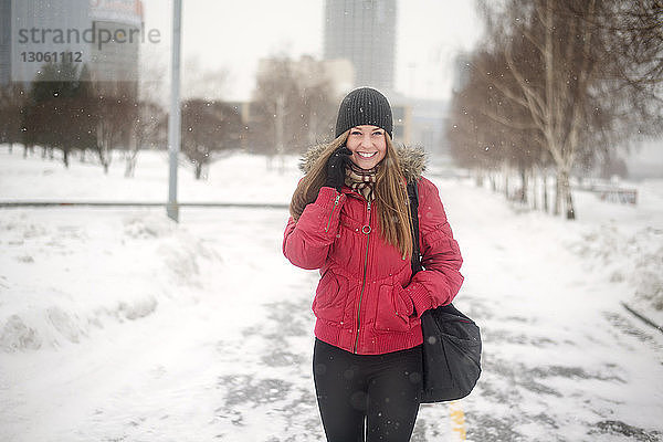 Glückliche junge Frau  die im Winter beim Gehen auf der Straße mit dem Handy telefoniert