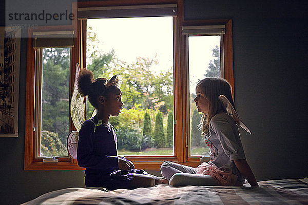 Seitenansicht von Mädchen in Feenkostüm  die zu Hause auf dem Bett sitzen