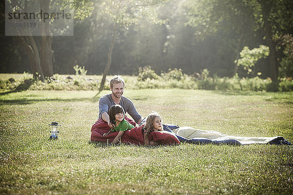 Lächelnder Mann schaut Kinder an  während er auf dem Rasen sitzt
