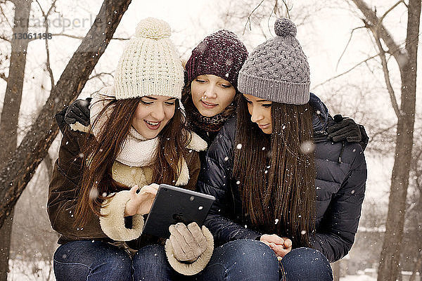 Freunde benutzen digitales Tablet im Park bei Schneefall