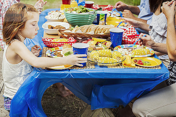 Mädchen isst  während sie mit der Familie am Picknicktisch sitzt