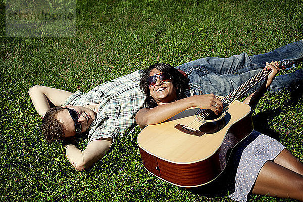 Hochwinkelaufnahme eines Paares mit Gitarre auf einem Grasfeld liegend